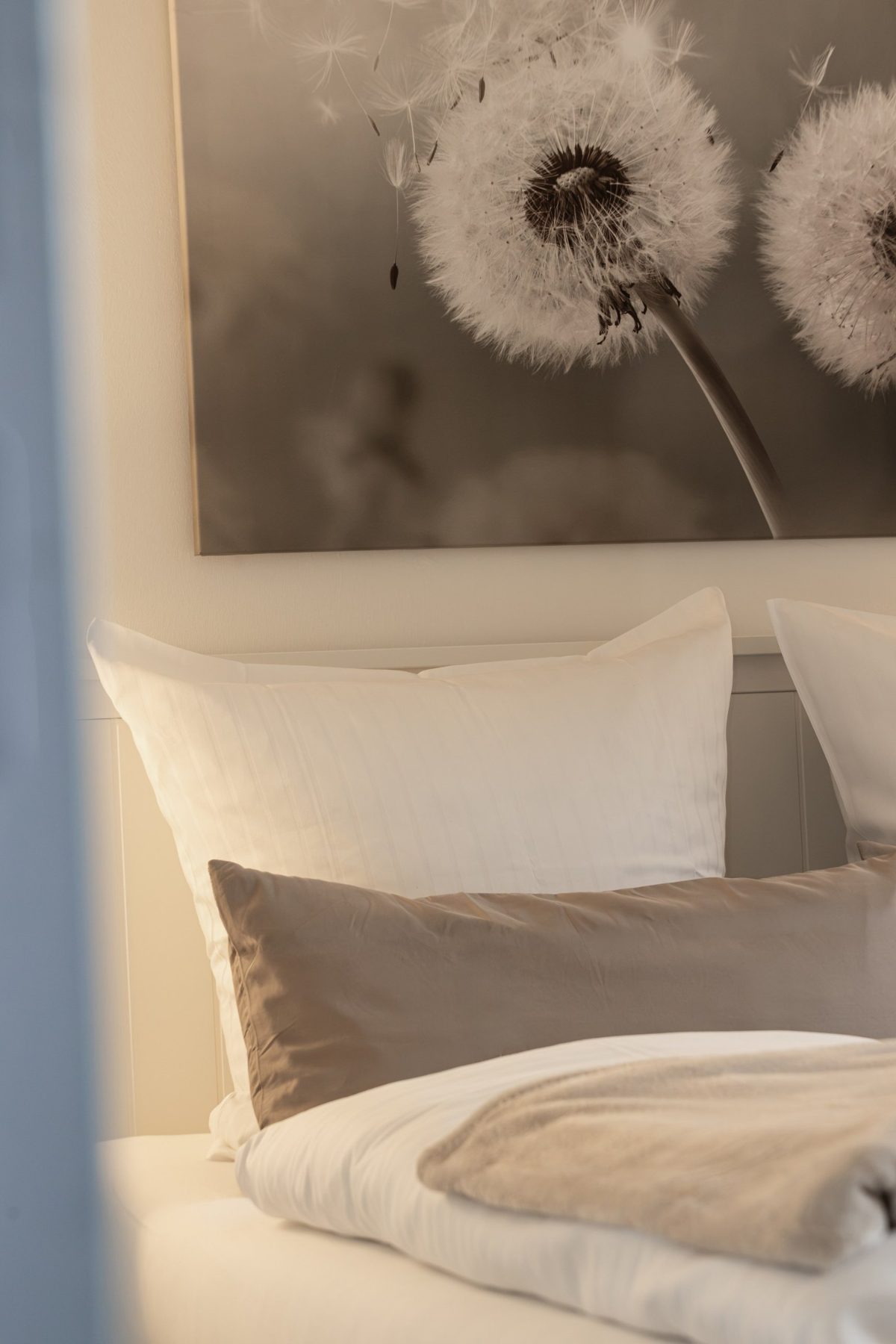 Bett mit weißen Kissen unter einem Pusteblumen-Bild