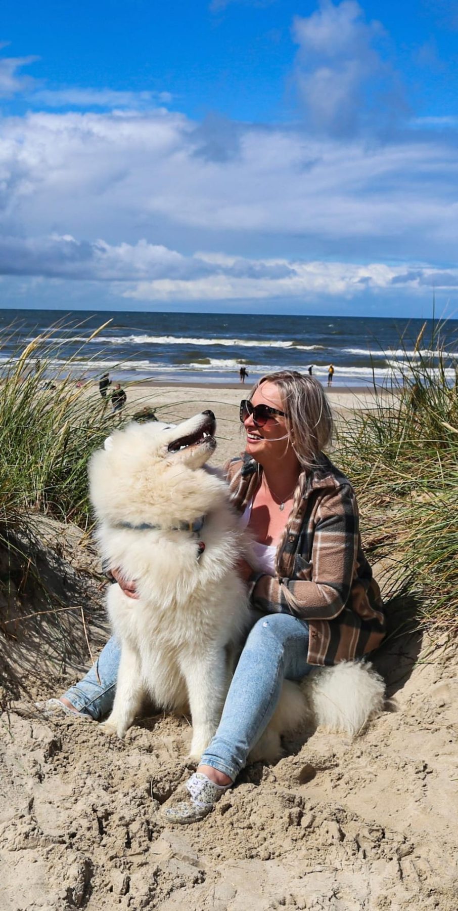 Moni Schuchardt lachend mit ihrem weißen Hund in den Dünen am Meer