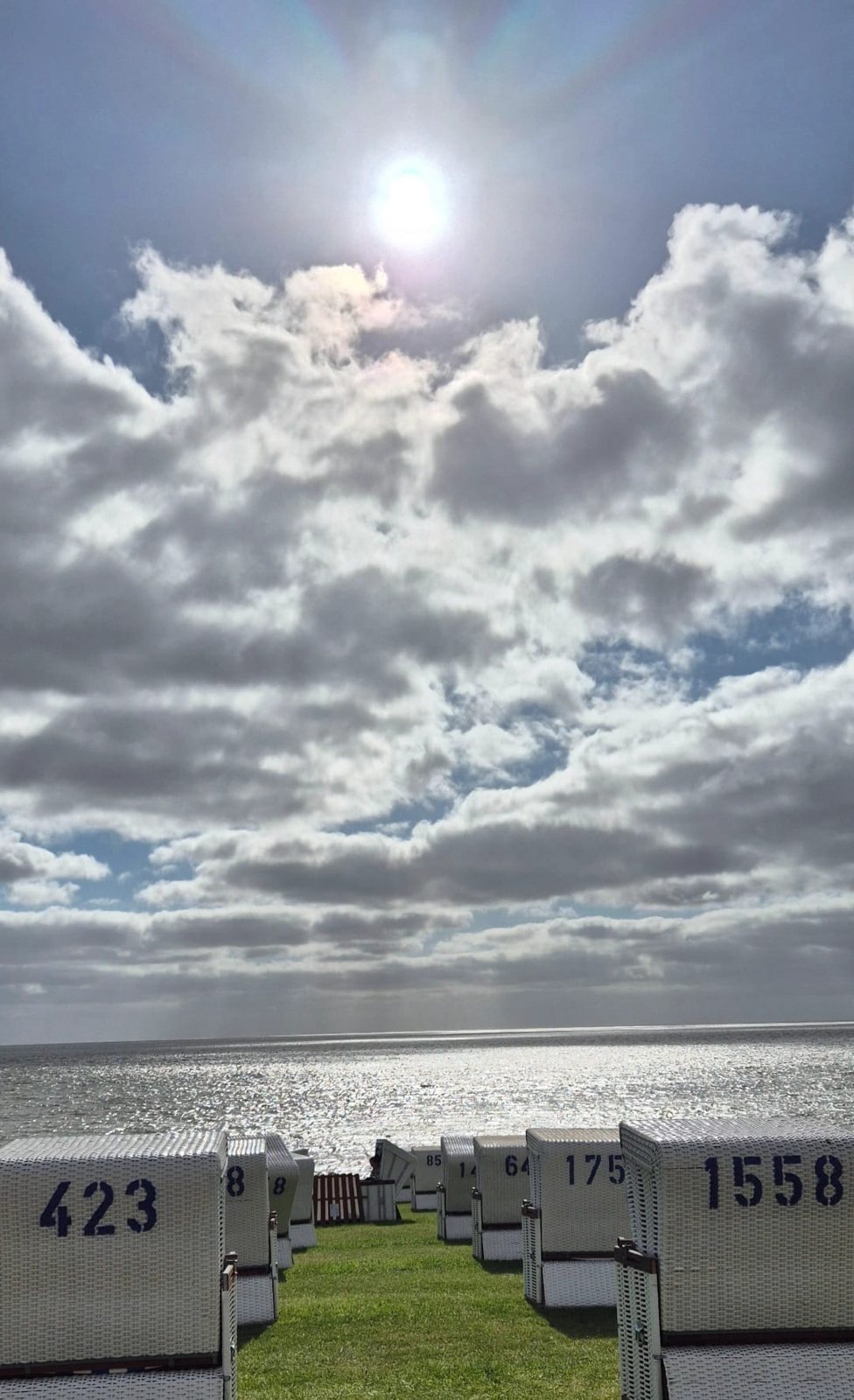 Strandkörbe auf dem grünen Deich vor der glitzernden Nordsee unter Wolkenhimmel